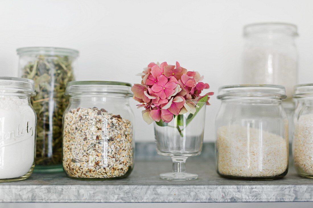 Storage jars (old preserving jars) with muesli, rice, verbena leaves and flour on a zinc shelf in the kitchen