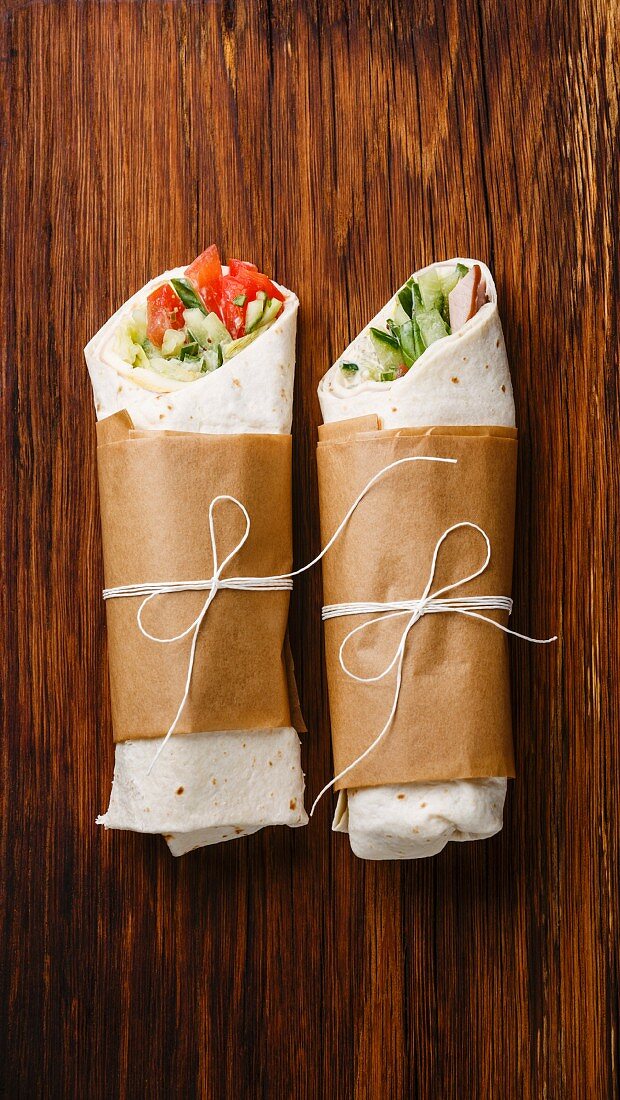 Tortilla wraps sandwiches with fresh vegetables on wooden background