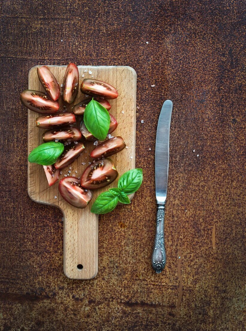 Fresh tomato slices with salt and basil leaves on wooden chopping board