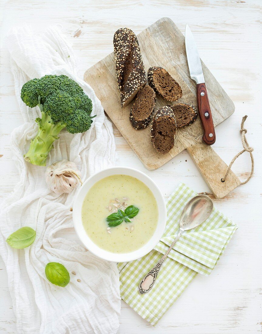 Homemade broccoli cream soup in white bowl with fresh rye baguette on wooden board