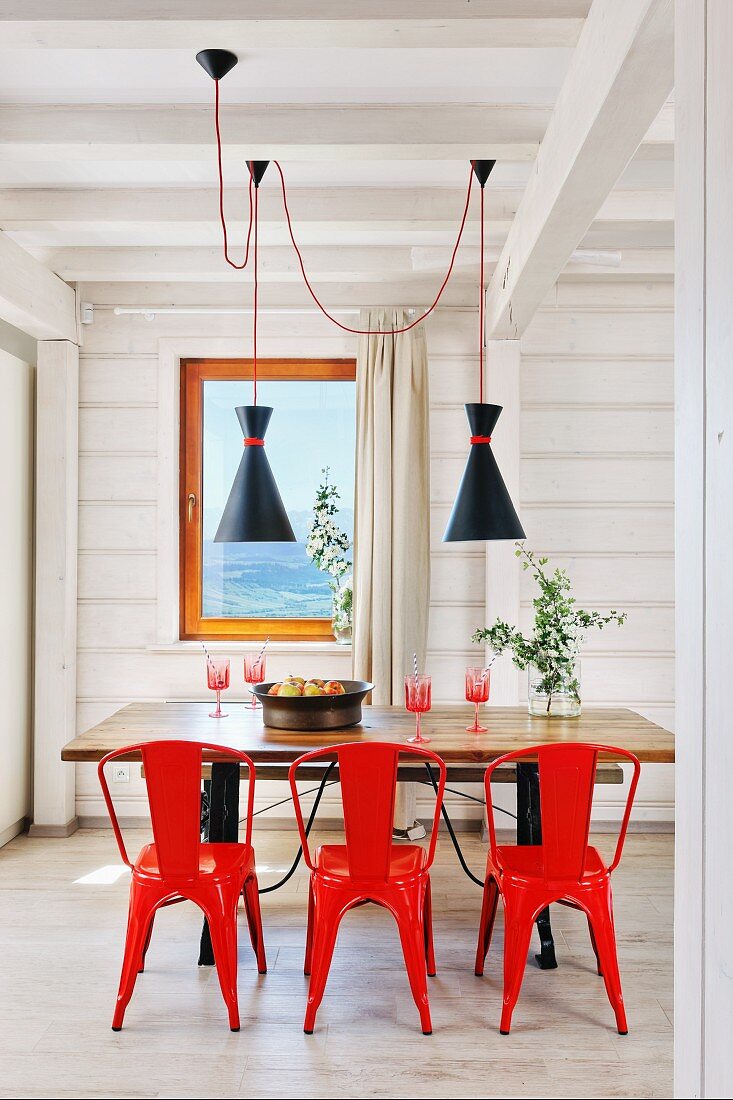 Red metal chairs around wooden table in white wooden house