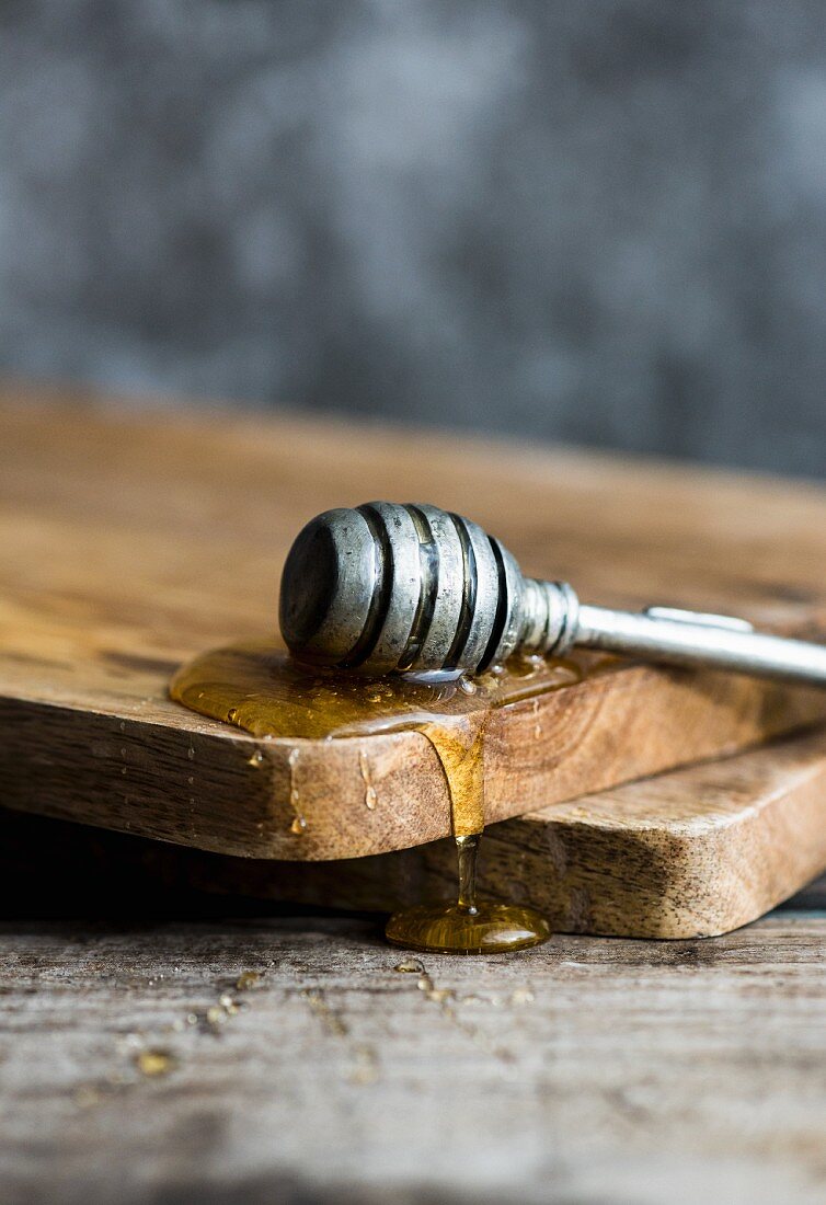 A honey dipper with honey on a wooden board