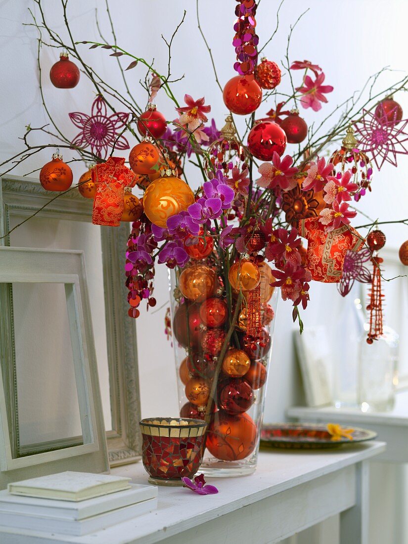 Christmas arrangement of orchids and baubles in shades of red, orange and purple