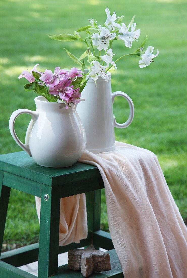 Krugvasen mit Blumen auf grüner Trittleiter im Garten