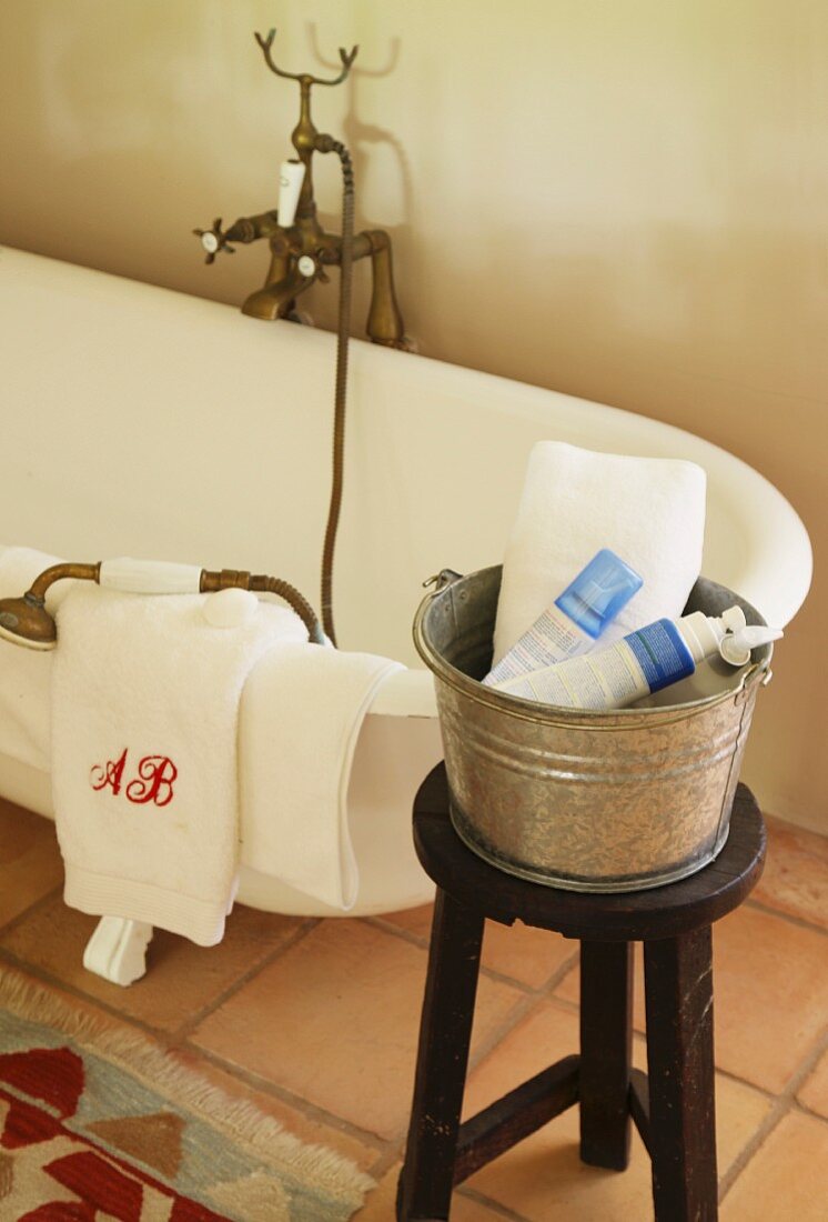 Vintage bath taps on free-standing white bathtub, monogrammed towels and zinc bucket on stool