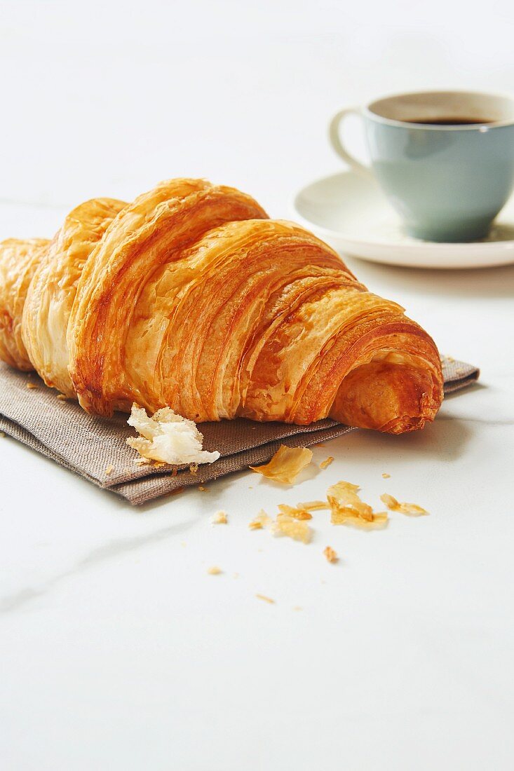A croissant with an espresso cup in the background