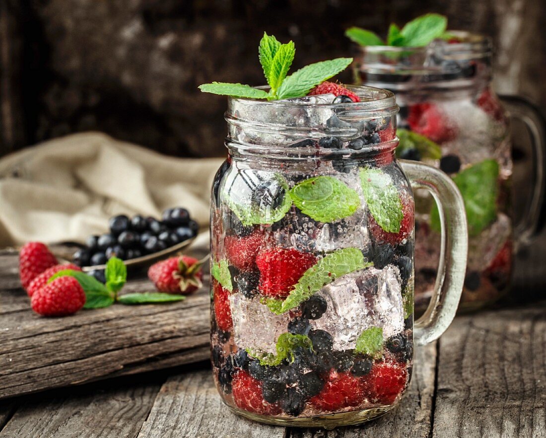 Detox-Drink mit frischen Beeren, Minze und Eiswürfeln im Glas auf Holzuntergrund
