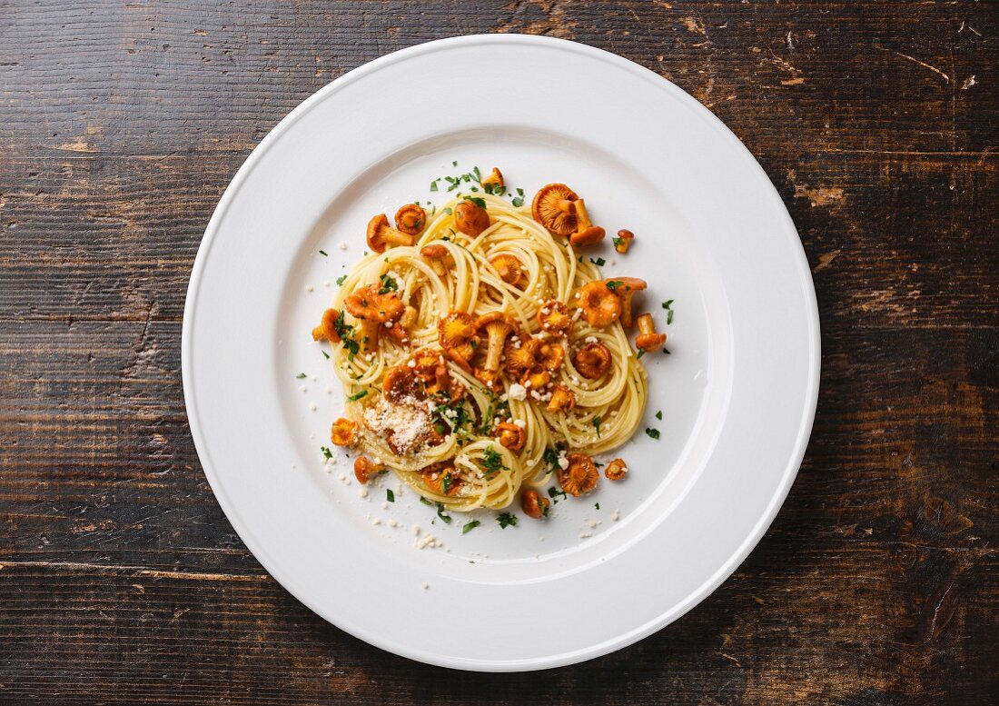Spaghetti mit Pfifferlingen auf weißem Teller auf Holztisch