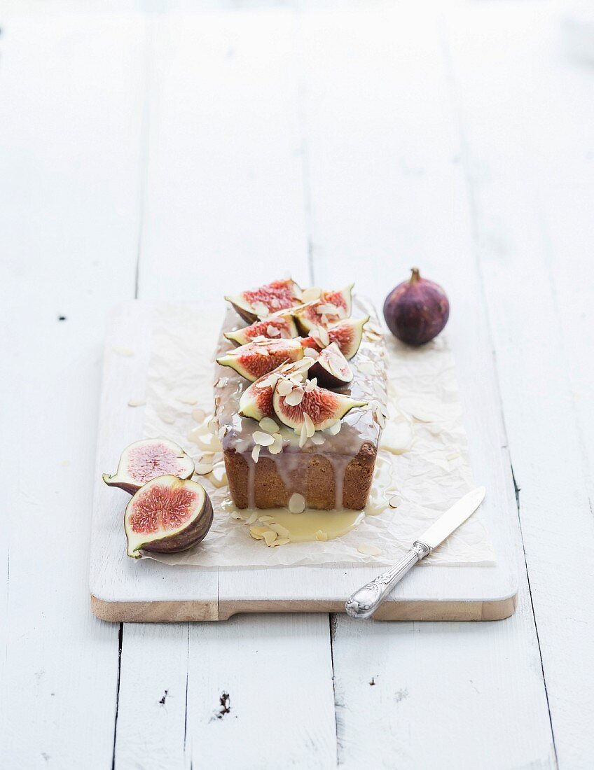 Kastenkuchen mit Feigen, Mandeln und weißer Schokolade auf weißem Holzbrett