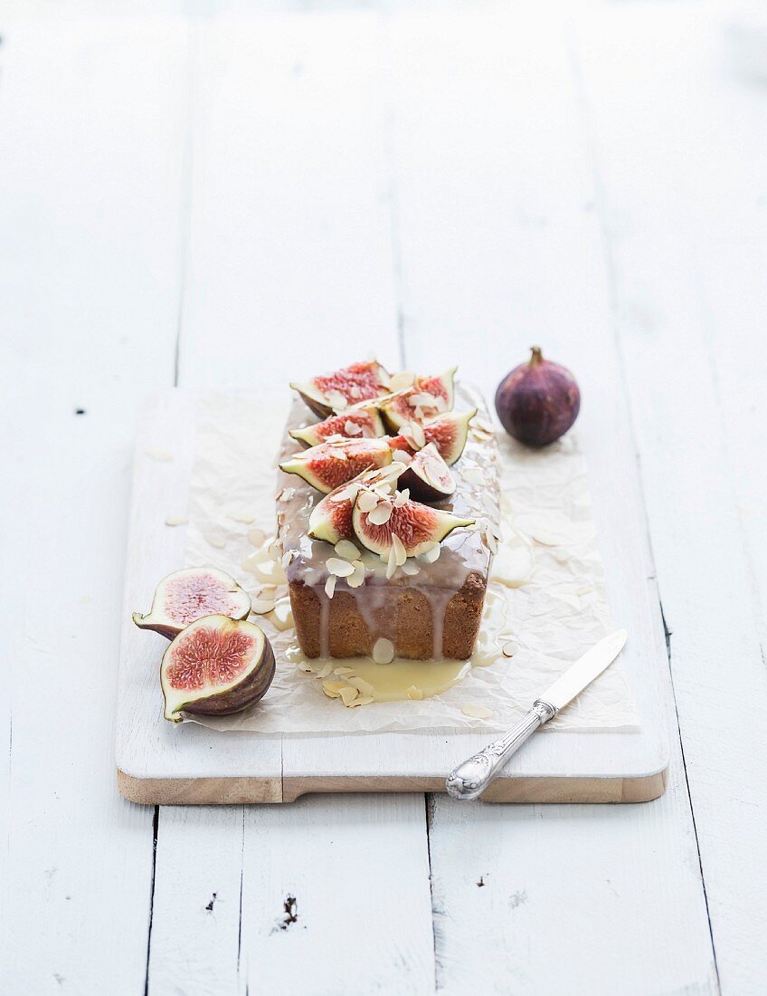Loaf cake with figs, almond and white chocolate on white serving board over white wooden background