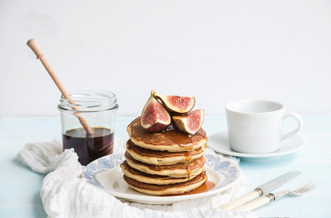 Homemade pancaces tower with fresh figs and honey on white plate over white wall background