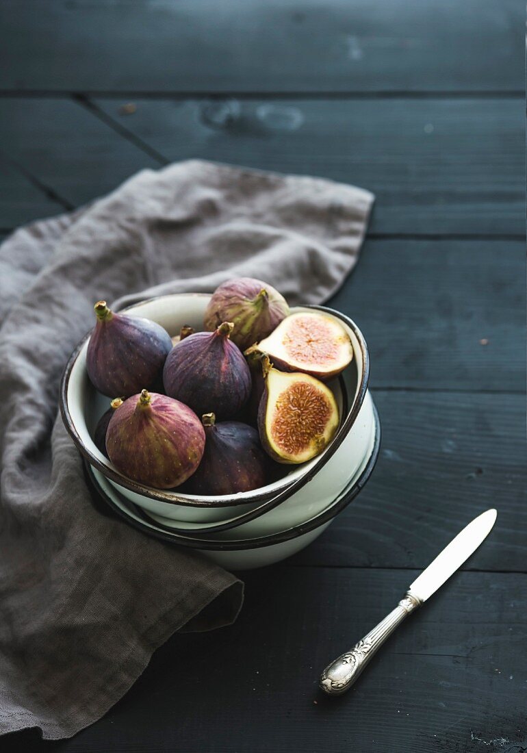 Fresh figs in white metal bowls over dark wooden background