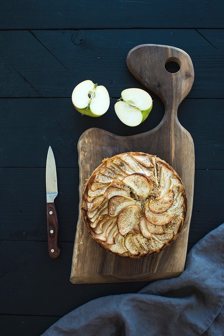 Homemade apple pie served with fresh apples on rustic wooden board over dark wooden backdrop