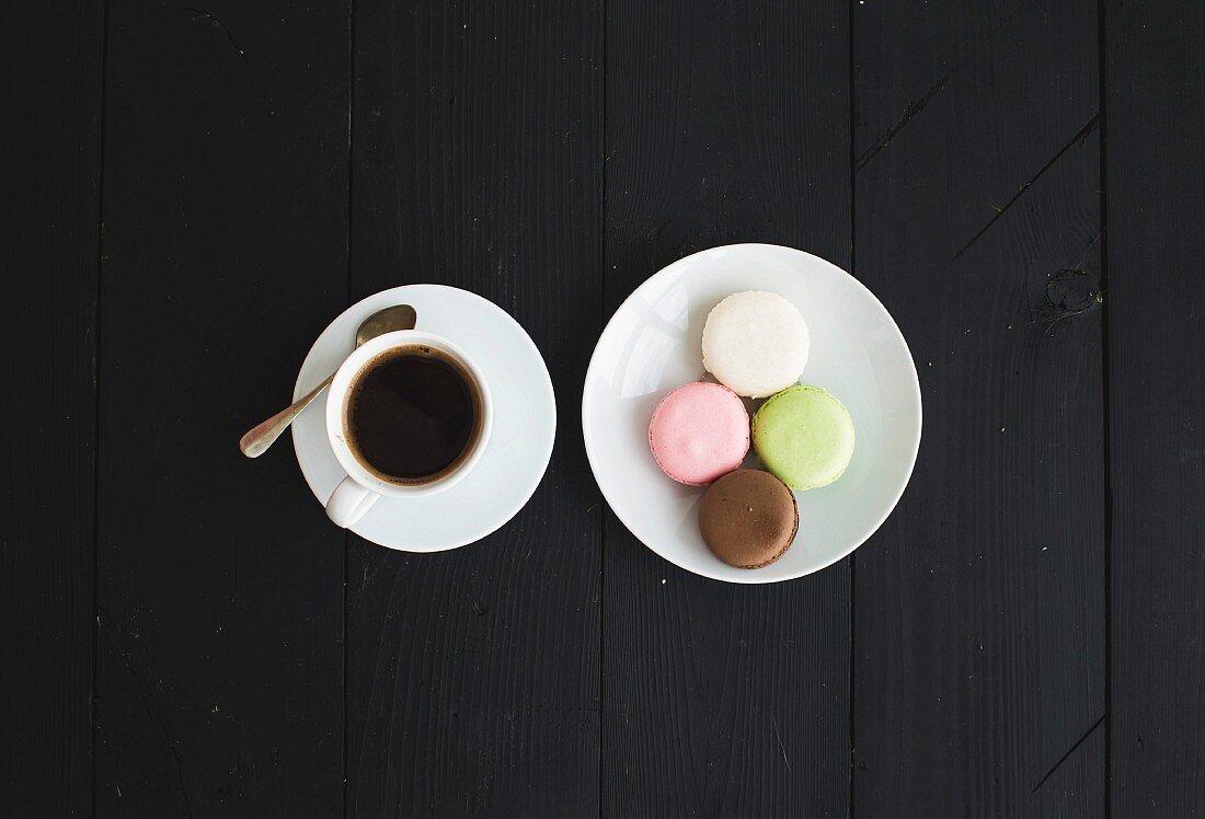 Eine Tasse Espresso und bunte Macarons auf schwarzem Holzuntergrund