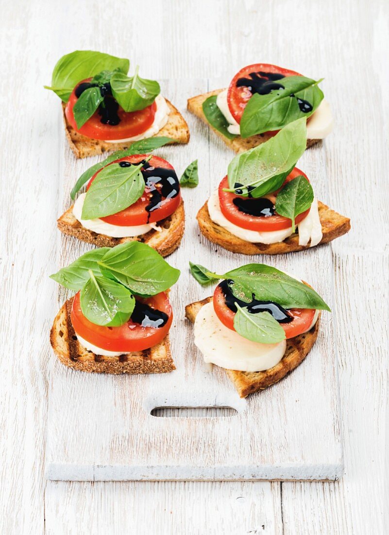 Toasted bread with tomato, mozzarella, basil and balsamic vinegar on a wooden board painted white