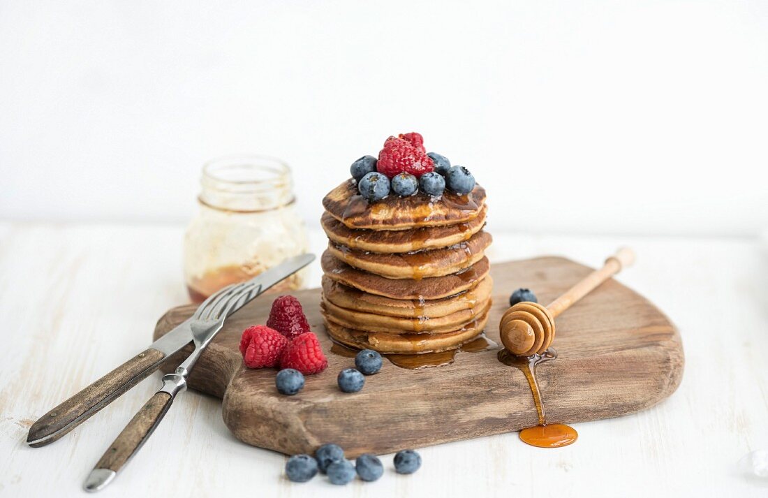 Homemade pancakes with fresh garden berries, honey on wooden board over white painted wooden background