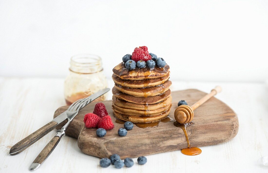 Turm aus Pancakes mit frischen Beeren und Honig auf Holzbrett
