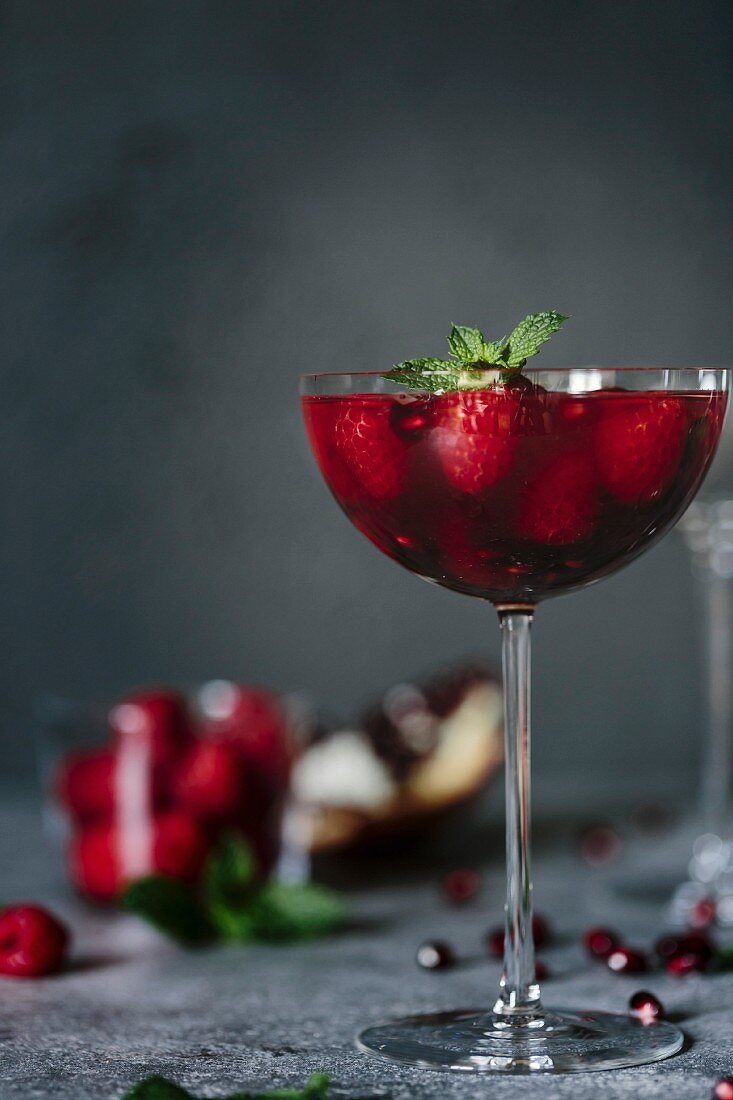 A coupe glass of Raspberry and Pomegranate Champagne Cocktailed garnished with mint