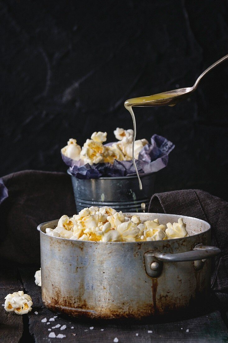Prepared buttered popcorn served with sea salt in small buckets and vintage aluminum pan on old wooden kitchen table