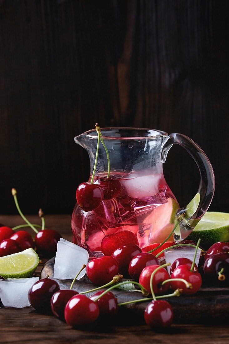 Limonade mit Kirschen und Limetten, serviert in Glaskanne mit Eiswürfeln