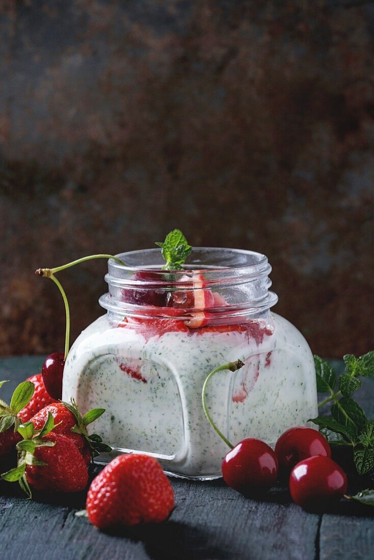 Square glass jar with homemade yogurt with mint, strawberry puree and cherry, served with fresh berries