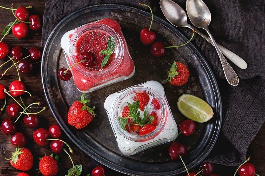 Two Square glass jars with homemade yogurt with mint, strawberry puree, cherry and chia seeds