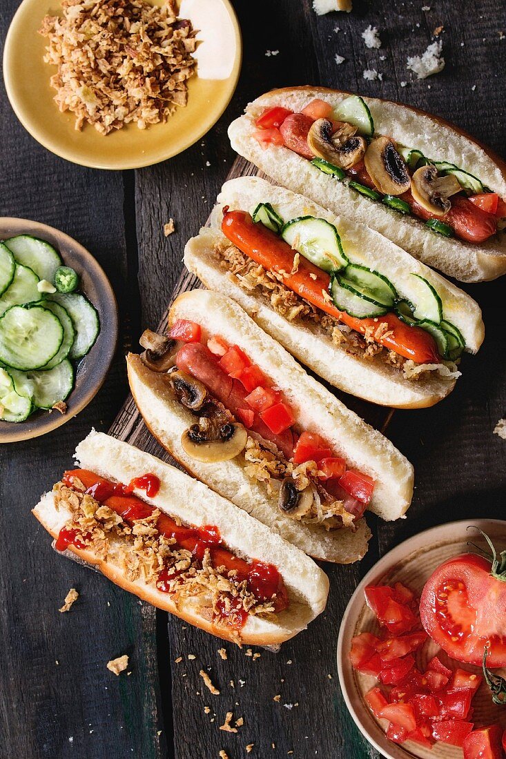 Selbst gemachte Hot Dogs mit gebratenen Zwiebeln, Tomaten und Gurken, daneben mit Zutaten