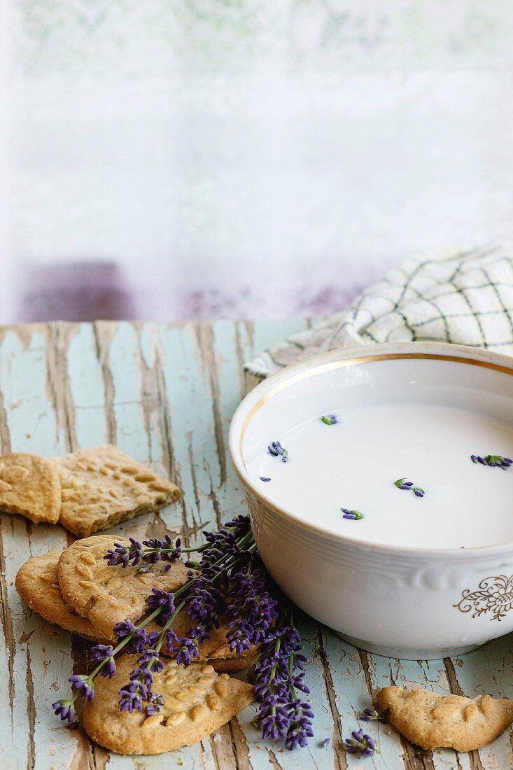 Lavender cookies and bowl of aromatic milk, served with kitchen towel on old wooden table