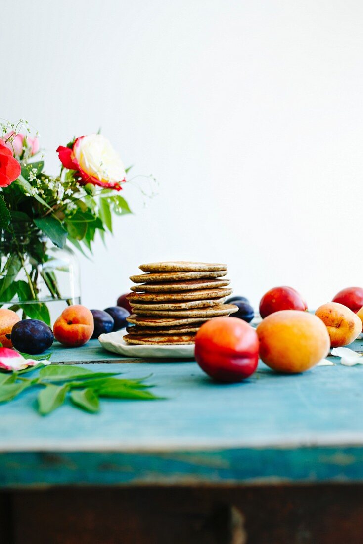 Gestapelte Pancakes umgeben von Früchten auf türkis Holztisch