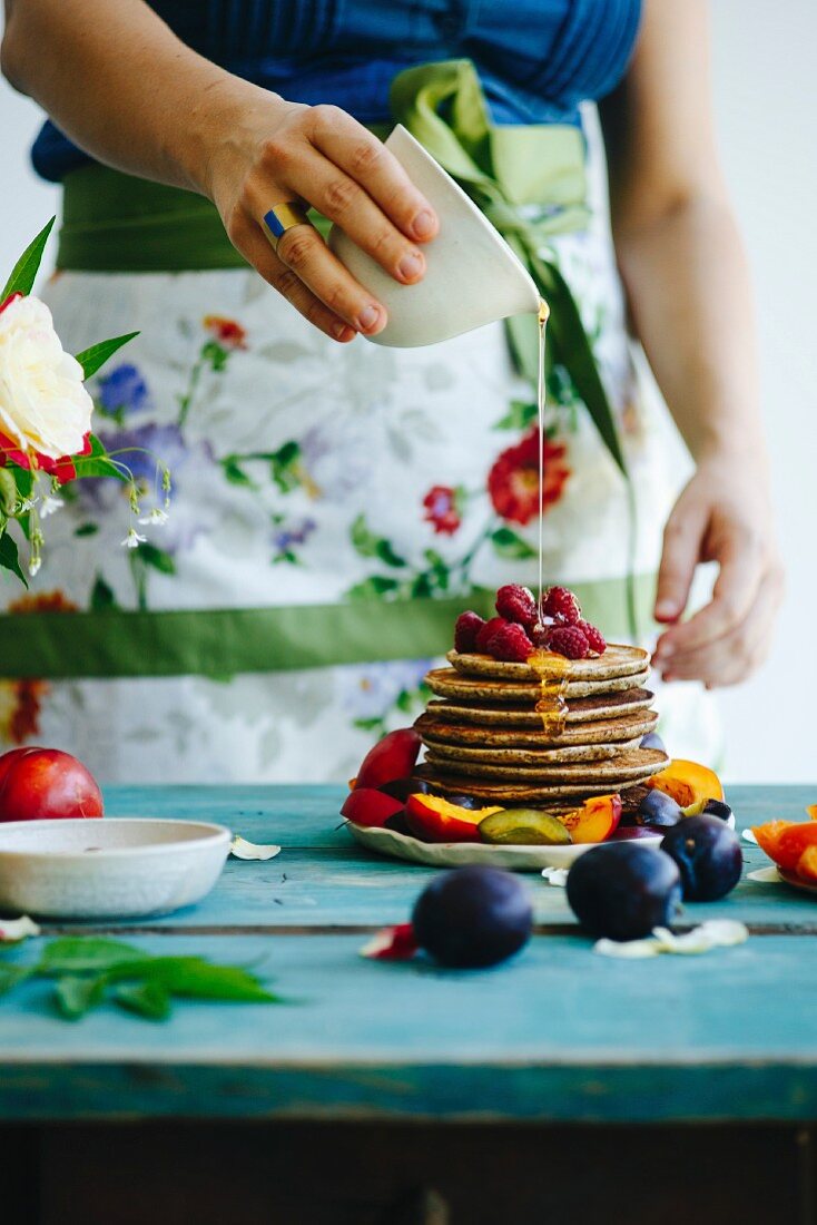 Girl with flower apron pours honey over pancakes