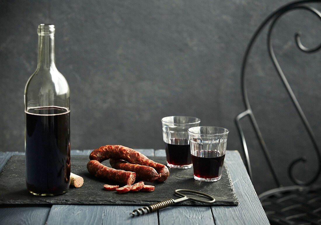 A table scene with red wine and chorizo