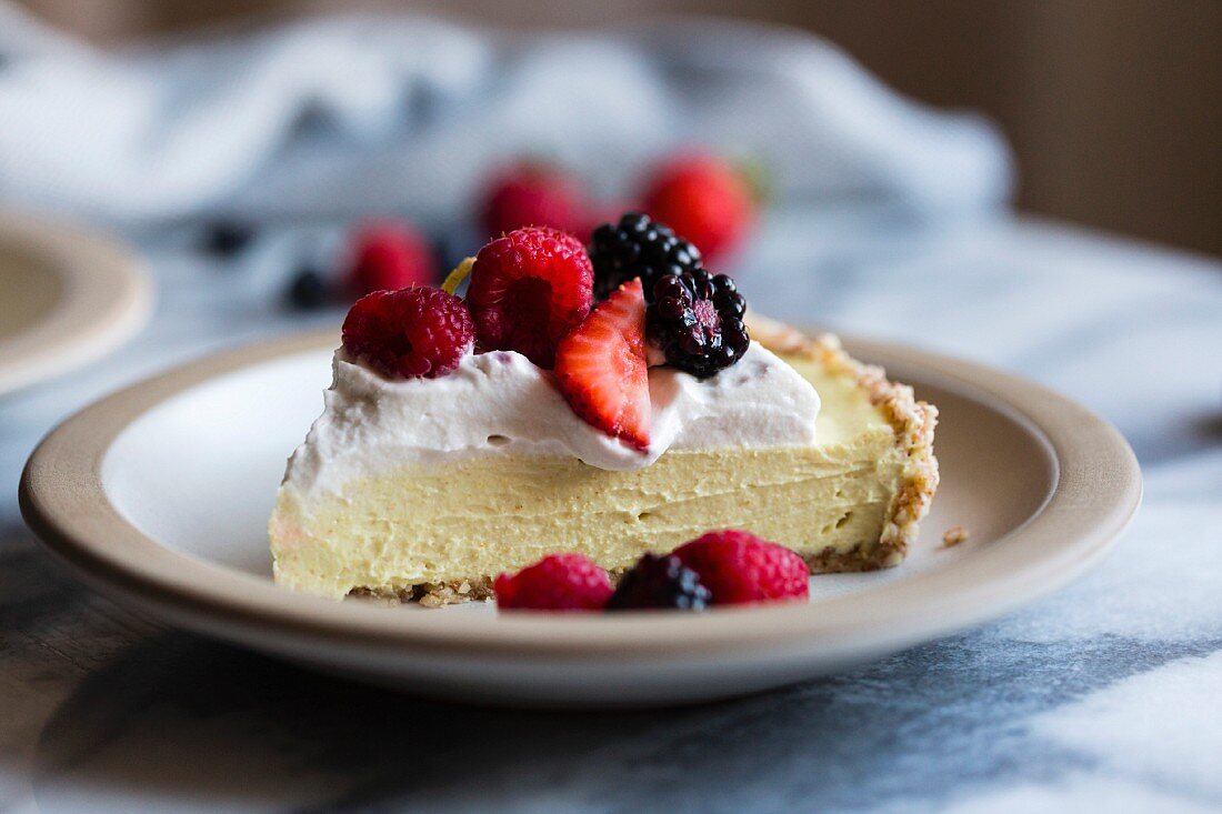 Ein Stück Kühlschranktorte mit Zitronencreme, Kokosmilchsahen und frischen Beeren (vegan, glutenfrei, raffinierter Zucker frei) auf Teller