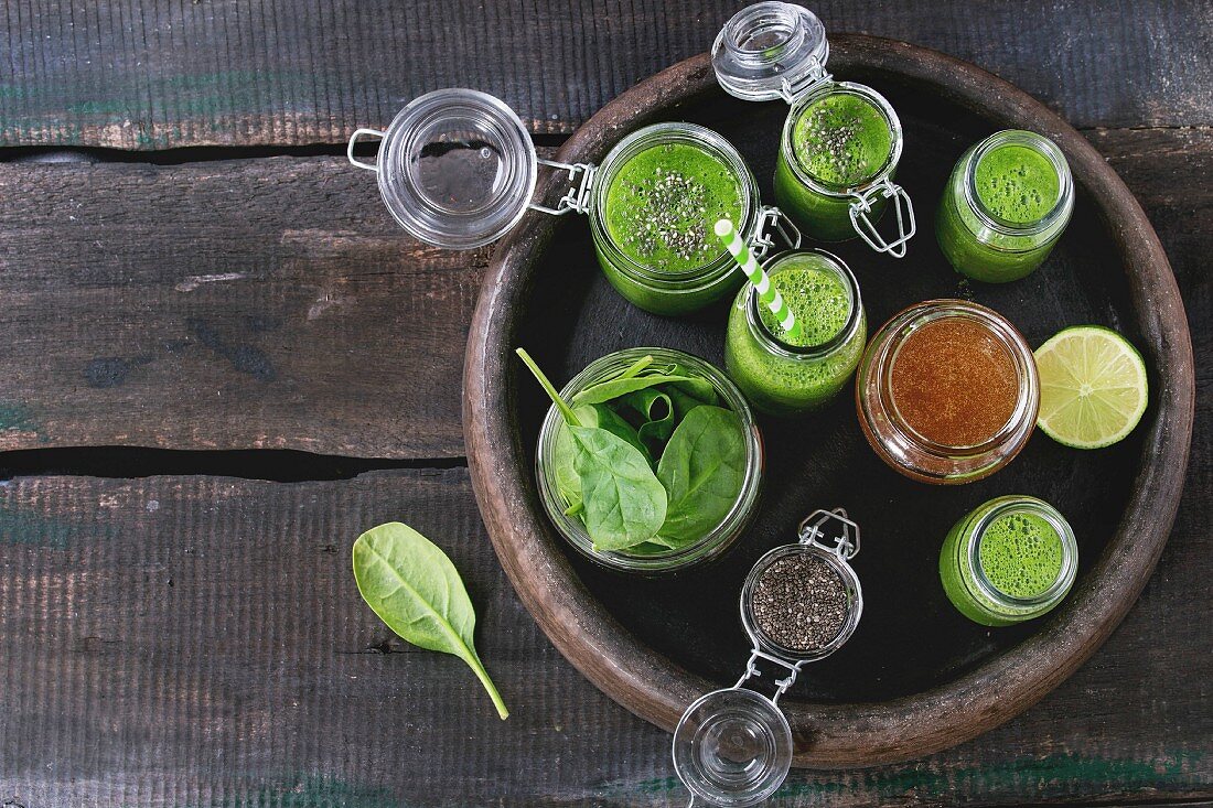Spinach smoothie in glass jars served with spinach leaves, chia seeds, honey and lime