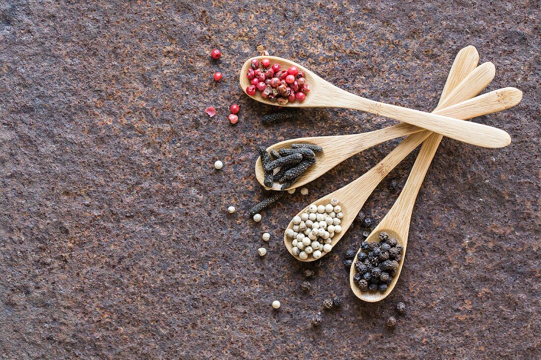 Four different types of pepper on wooden spoons