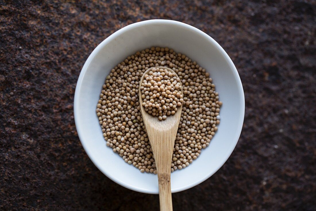 Mustard seeds with a wooden spoon in a bowl (seen from above)