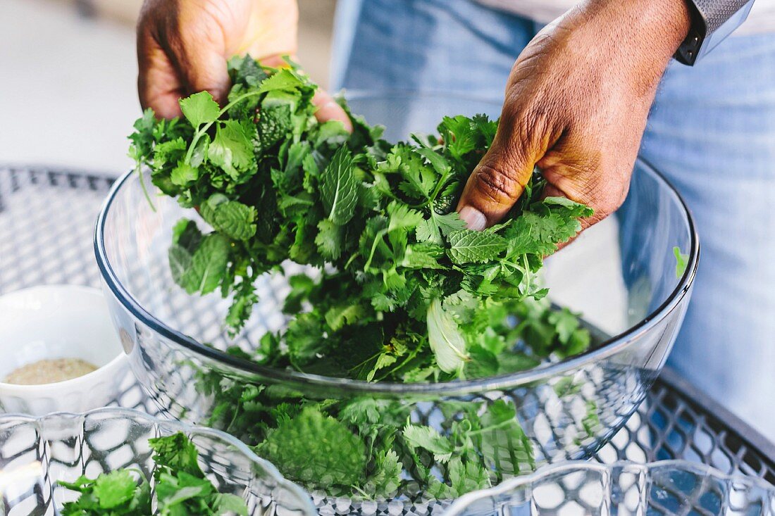 A man is mixing fresh mint and prepping it for the Thai grilled beef salad