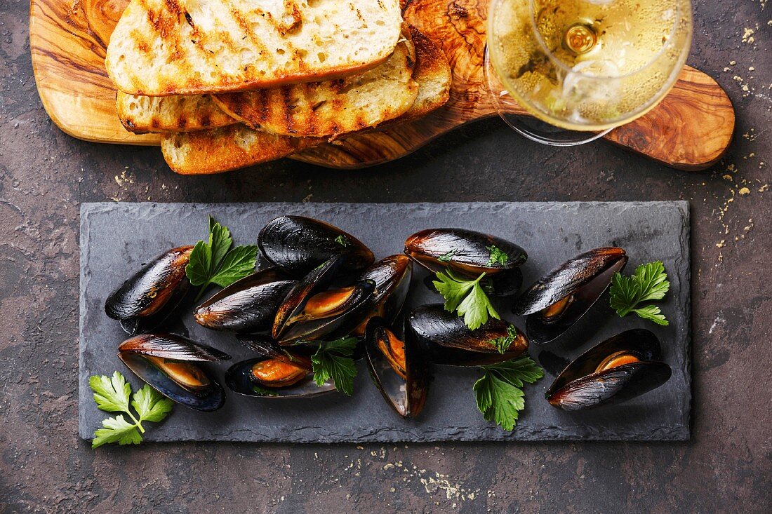 Mussels on stone slate, Bread toasts and Wine on dark background