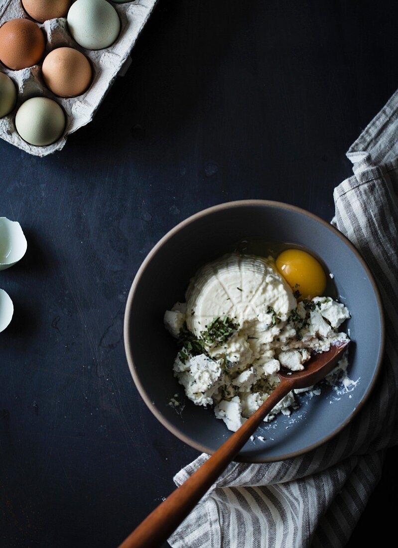 Ricotta soft cheese in a mixing bowl with eggs and herbs