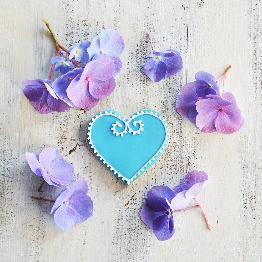 Keks in Herzform mit blauem und weißem Zuckerguss dekoriert, umgeben von Blumen