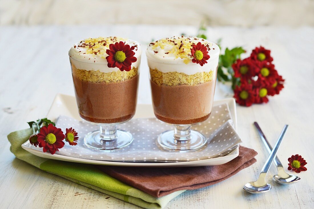 Dessert in zwei Gläsern nebeneinander mit Schokolade, Frühstücksflocken und Kokosmilch, mit frischen Blumen dekoriert