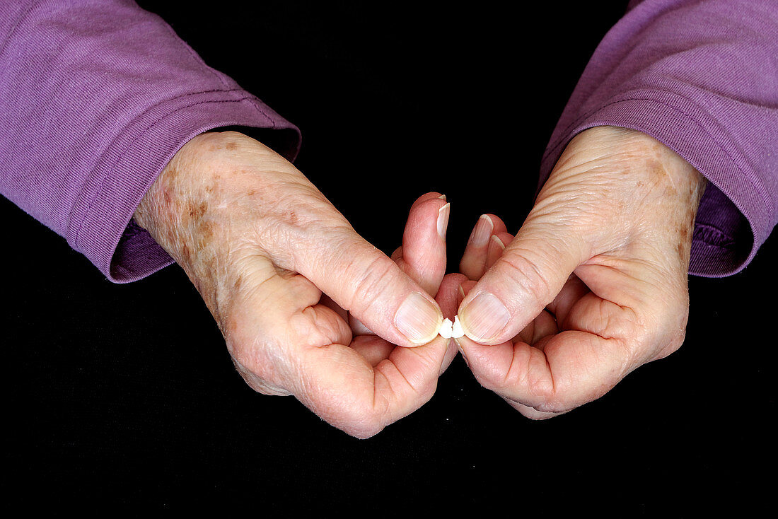 Elderly hands break a pill