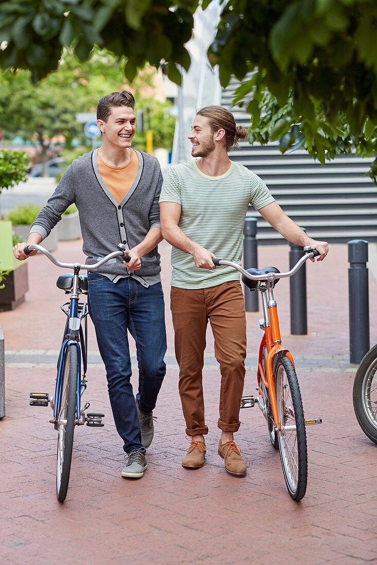 Two young men pushing bicycles