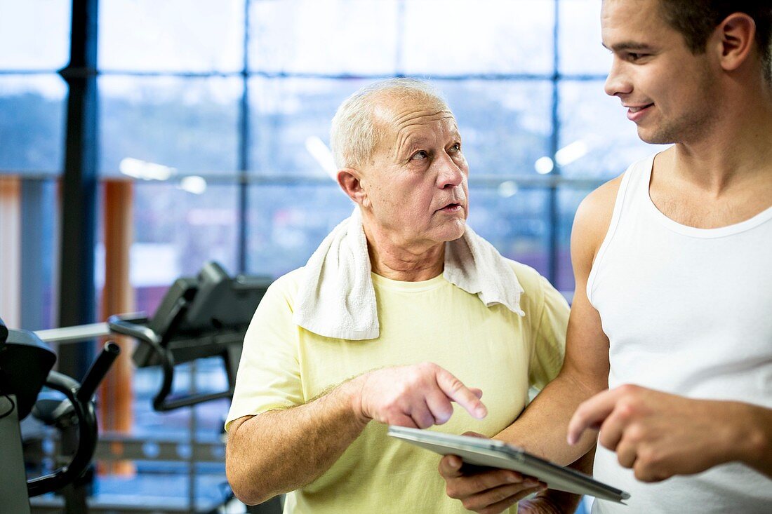 Gym trainer showing tablet to senior man