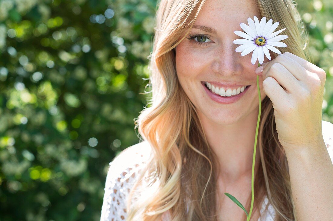 Woman holding daisy in front of eye