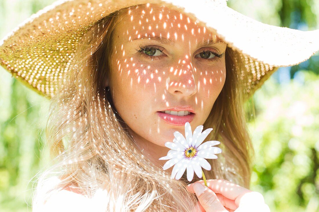 Woman wearing sunhat holding daisy