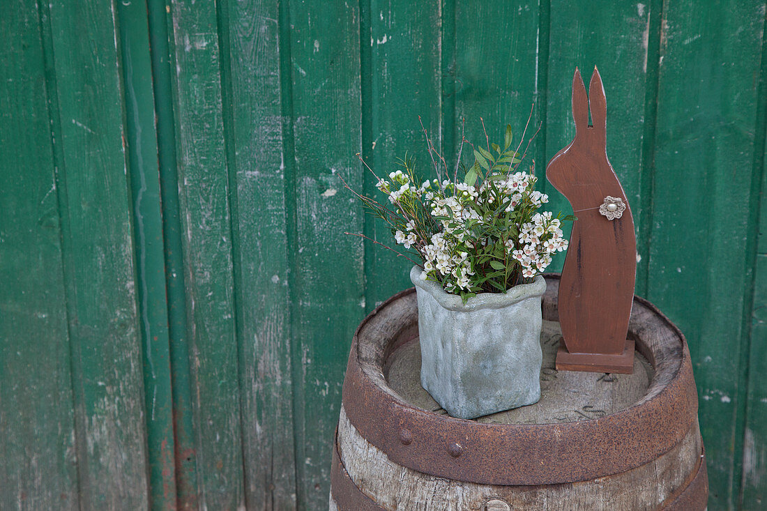 Sträußchen mit Wachsblumen und Dekohase auf einem Holzfass