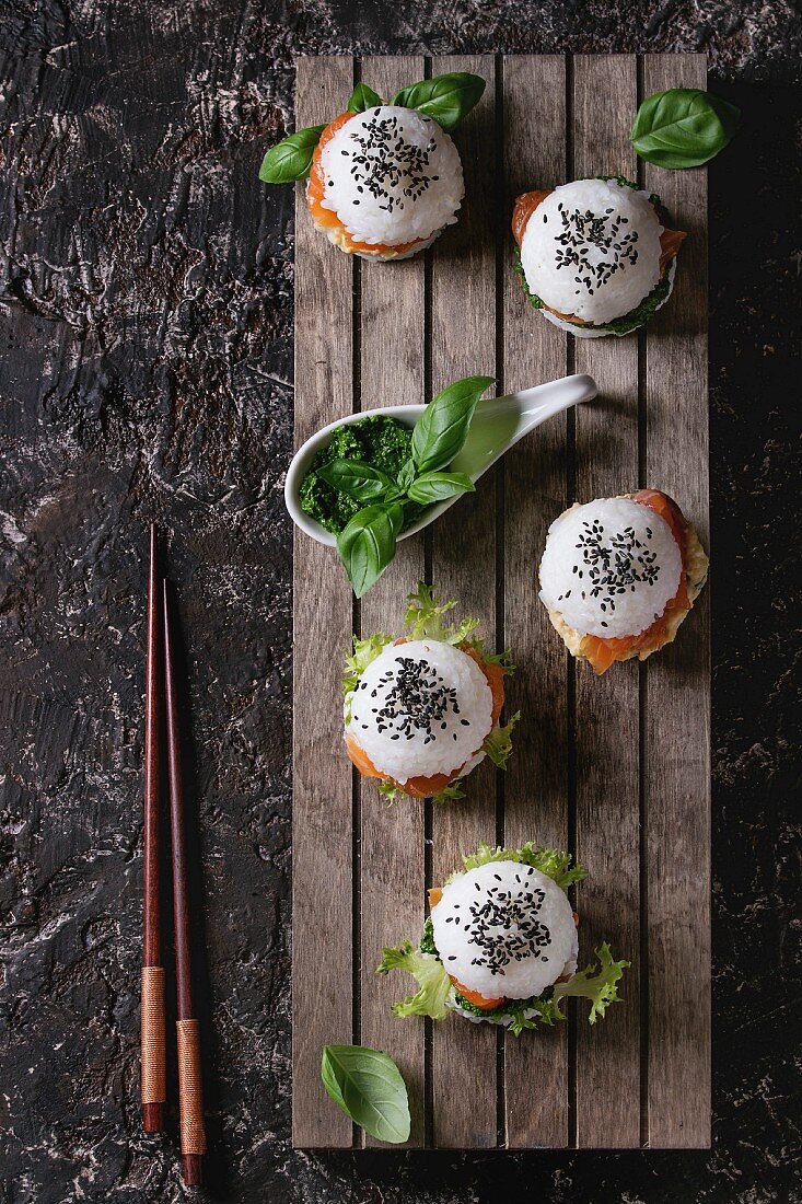 Mini rice sushi burgers with smoked salmon, green salad and sauces, black sesame served on wood pallet tray