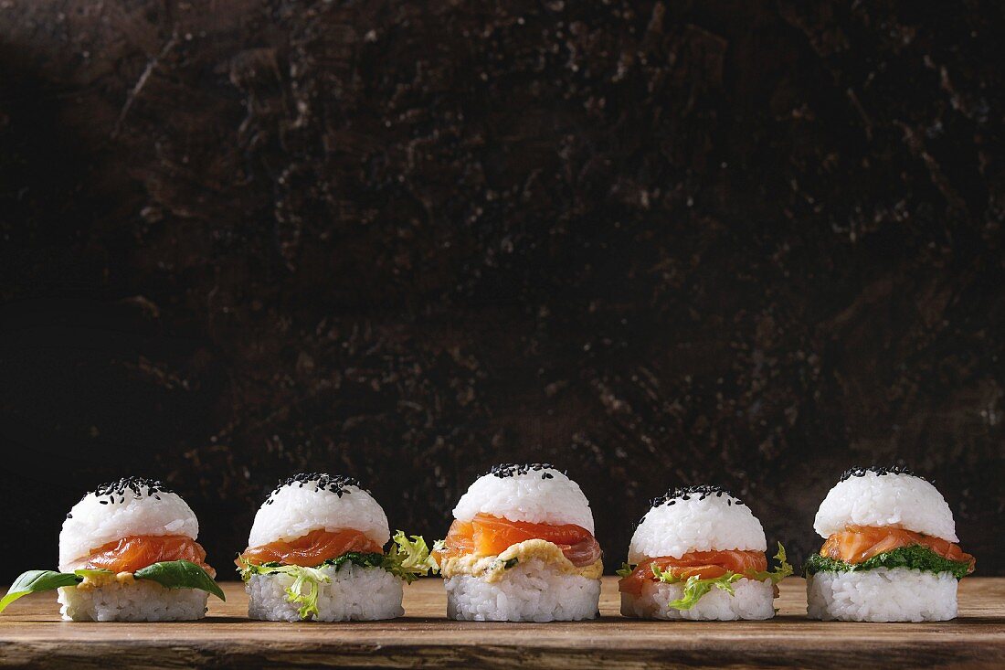 Mini rice sushi burgers with smoked salmon, green salad and sauces, black sesame served with wooden chopsticks
