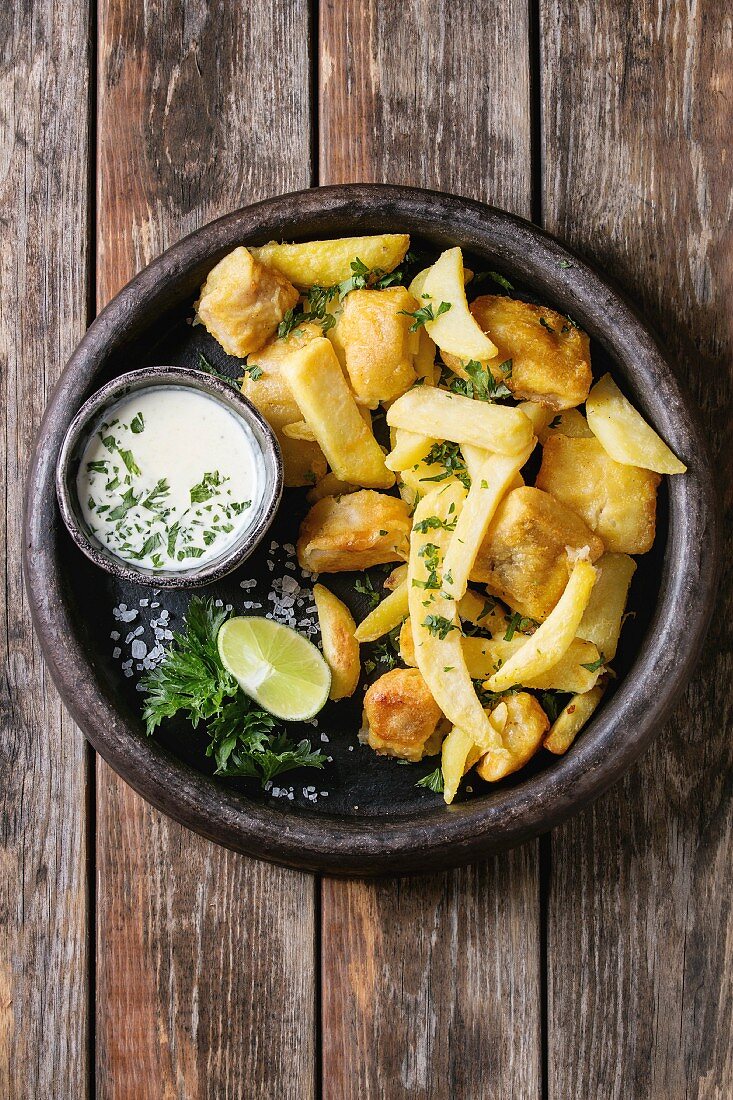 Traditional british fast food fish and chips, served with white cheese sauce, lime, parsley, french fries