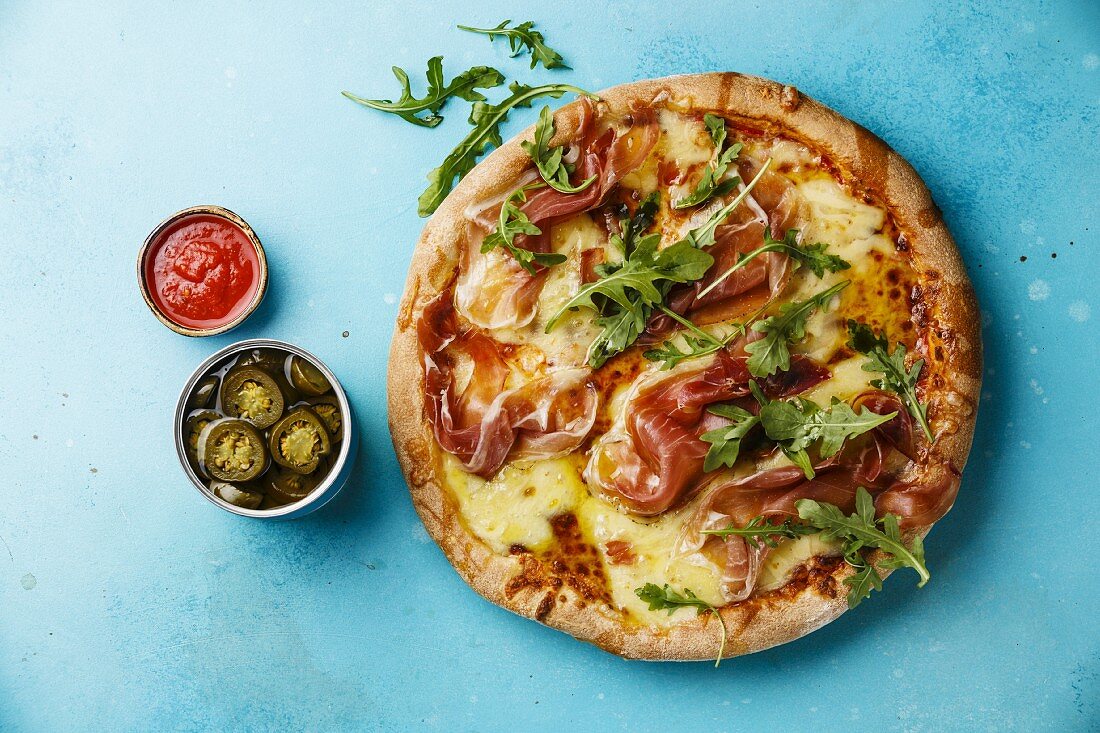 Pizza mit Mozzarella, Prosciutto und Rucola vor blauem Hintergrund